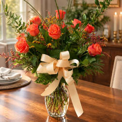 Coral roses in a clear glass vase with a cream ribbon bow