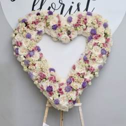 Heart-shaped floral wreath of cream, pink, and purple blooms on an easel