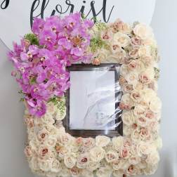Floral frame of pink orchids and cream roses around a photo opening