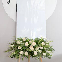White rose arrangement on a wooden easel with greenery