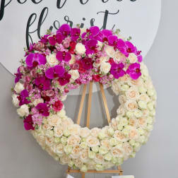 Large floral wreath with cream roses and bright pink orchids on a wooden easel