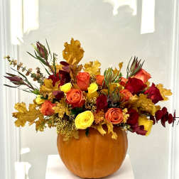 Autumn floral arrangement in a pumpkin vase with red, orange, and yellow roses