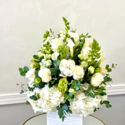 White floral arrangement in a ribbed white vase with green accents