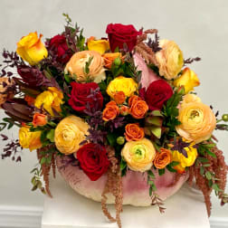 Mixed roses and ranunculus arranged in a pink pumpkin vase