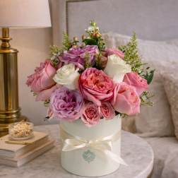 Pink and white roses arranged in a round white box with a ribbon