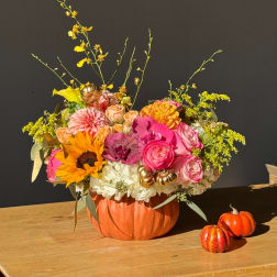 Mixed flower arrangement in a pumpkin-shaped container with small decorative pumpkins