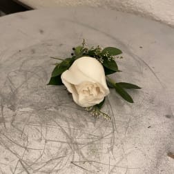 Single white rose boutonniere with greenery on a gray scratched surface