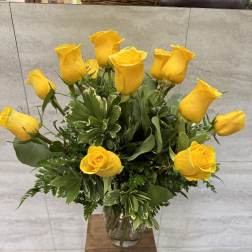Tall arrangement of yellow roses in a clear glass vase on a wooden stand.