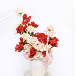 Bouquet of red and cream roses in a white vase with pink ribbons