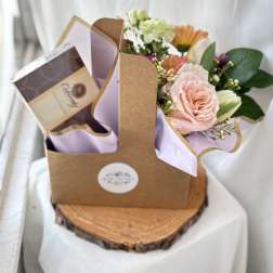 Gift caddy with pastel mixed flowers and a box of chocolates on a wood slice base.