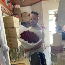 Man holding a large bouquet of red roses wrapped in white paper.