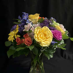 Mixed bouquet of roses, daisies, and purple flowers in a glass vase