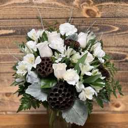 White floral arrangement in a glass vase with lotus pods and silver foliage