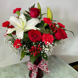 Red roses and white lilies in a dark vase with a heart ribbon
