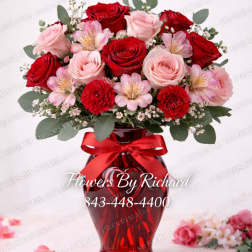 Red and pink roses arranged in a red glass vase with a ribbon.