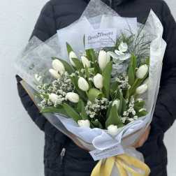 White tulips arranged in a wrapped bouquet with a yellow ribbon