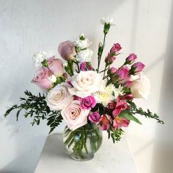 Pink and white roses with small white blooms in a clear glass vase.