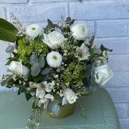 White roses and ranunculus in a gold vase with green accents