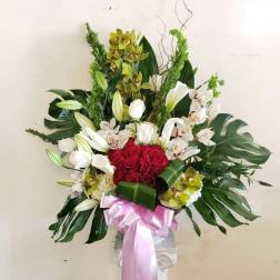 Large floral arrangement with red roses, white orchids, and lilies in a pedestal vase