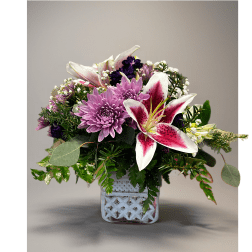 Pink lilies and lavender mums arranged with white filler flowers in a white cube vase