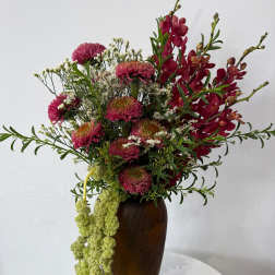 Tall bouquet of magenta flowers and red orchids in a brown vase