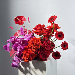 Red and purple floral arrangement with roses and gerbera daisies in a white pedestal vase