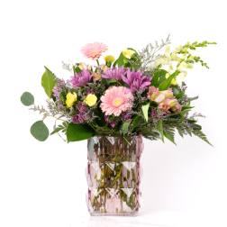 Mixed bouquet of pink gerbera daisies, purple mums, and yellow roses in a pink textured glass vase