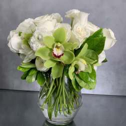 White roses and green orchids arranged in a clear glass vase