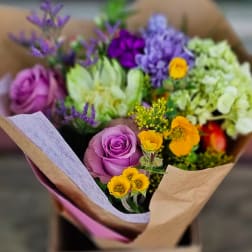 Bouquet of purple roses, yellow blooms, and pale green flowers wrapped in paper