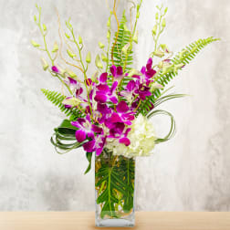 Purple orchids and white hydrangea in a clear rectangular vase