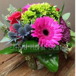 Bright mixed bouquet with pink gerbera daisies and blue thistle in a glass vase
