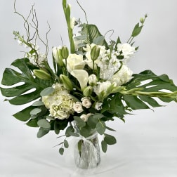 White floral arrangement in a clear glass vase with large green leaves
