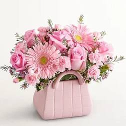 Pink roses and gerbera daisies in a pink handbag-shaped container