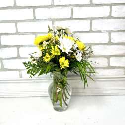 Small bouquet of yellow and white daisies arranged with greenery in a clear glass vase