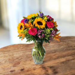 Mixed bouquet of sunflowers, roses, and lilies in a glass vase