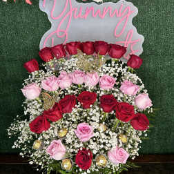 Pink and red roses arranged around a "Yummy" sign on a green backdrop