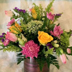 Mixed bouquet of pink, yellow, and purple flowers in a glass vase