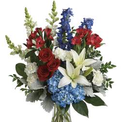 Mixed bouquet of red roses, white lilies, blue hydrangeas, and red alstroemeria in a glass vase