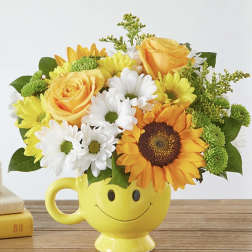 Yellow mug vase with a smiley face holding yellow and white flowers