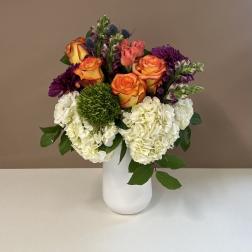 Bouquet of orange roses, white hydrangeas, and purple flowers in a white vase