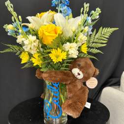 Bouquet of yellow and white flowers in a glass vase with a teddy bear