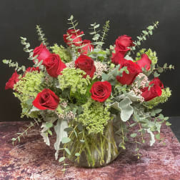 Red roses arranged in a glass vase with eucalyptus and green filler