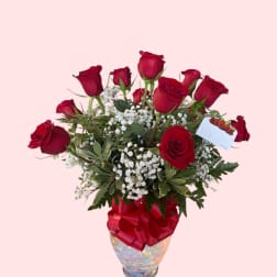 Red roses arranged in a glass vase with a red ribbon