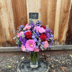 Mixed bouquet of pink, red, and purple flowers in a glass vase