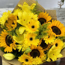 Bouquet of yellow sunflowers and lilies wrapped in newspaper-style paper