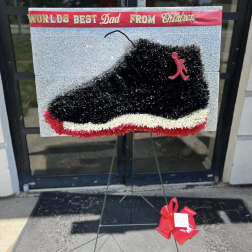 Black sneaker-shaped floral tribute on a stand with a red bow