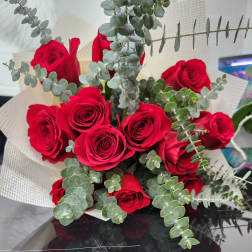 Hand-tied bouquet of red roses with eucalyptus accents wrapped in cream textured paper