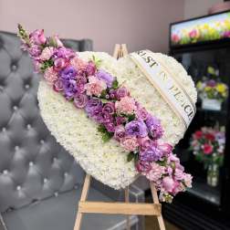 Heart-shaped floral tribute with pink and purple flowers on an easel