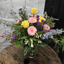 Mixed bouquet with yellow roses, pink gerbera daisies, and purple flowers in a glass vase