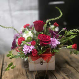 Mixed bouquet with red roses and purple flowers in a white box